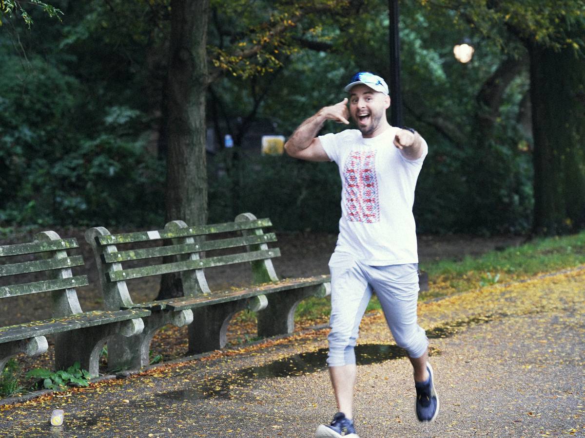 health wellness beginner running how to: woman jogging comfortably on a tree-lined path wearing proper running shoes and smiling